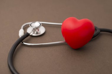Steteskop ve kahverengi bir arka plan üzerinde kırmızı lastik kalp