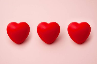 Pembe bir arka plan üzerinde üst üste üç kırmızı Kalpler