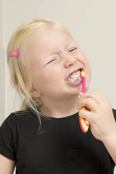 Маленькая девочка в черной рубашке чистит передние зубы — стоковое фото