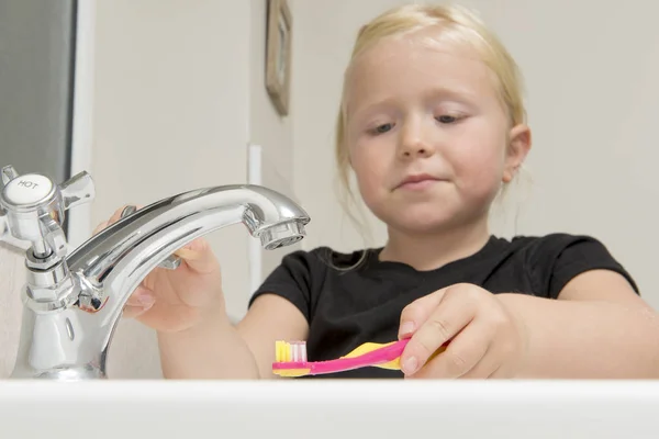 Маленькая девочка собирается вымыть зубную щетку в ванной раковине — стоковое фото
