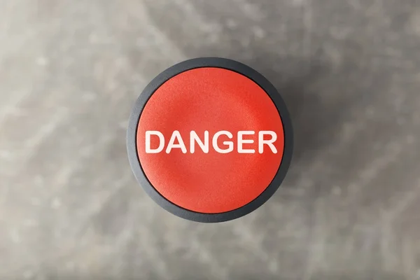 Накладка червоної кнопки'Небезпечно'Натисніть кнопку над розмитим сірим Backgroun — стокове фото