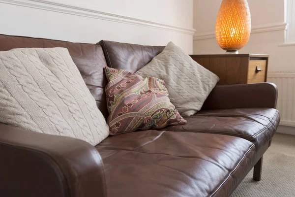 Sofá de couro marrom vintage com travesseiros ao lado da lâmpada de mesa — Fotografia de Stock