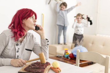 Mom on Phone While Preparing Meal as Kids Play in the Background clipart