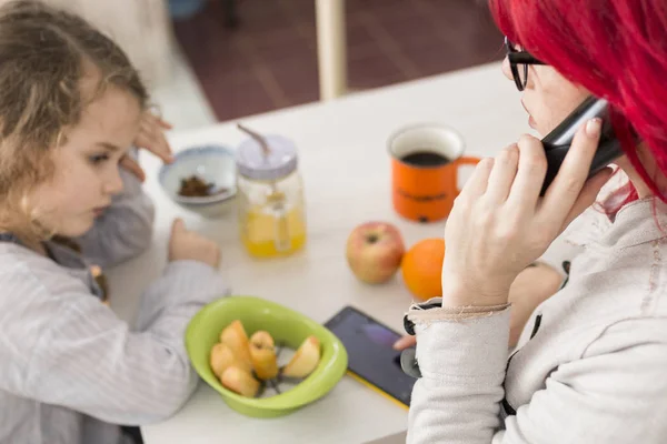 Mom on the Phone by Table of Snacks While Child Looks Bored