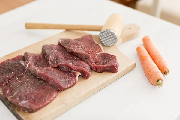 Trozos de carne cruda sazonada en la tabla de cortar de madera con zanahorias —  Fotos de Stock