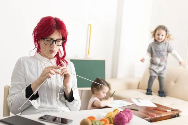 Mother Busy Knitting as Children Play in the Background