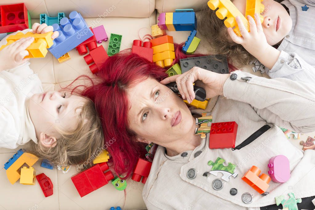 Exhausted Mom on Phone with Kids Lying on Plastic Bricks