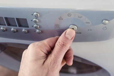 Bir çamaşır makinesi kontrol paneli üzerindeki bir düğmeye basarak başparmak