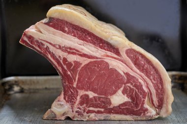 Yakından çekilmiş, pişmemiş sığır eti, alüminyum tepside dikilirken, siyah bir arka planda.