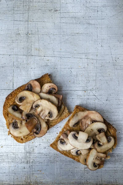 Mushrooms on toast servings on worn stainless steel background overhead view with copy space