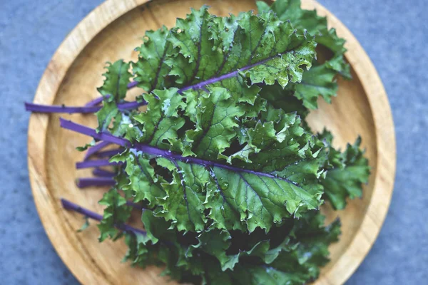 Kale leaves with purple stem and veins on wooden dish overhead shot