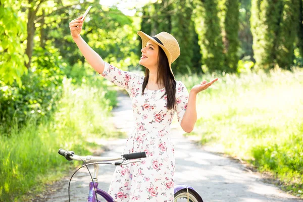 Happy pretty young girl bicycling and selfie on summer park. Happy relax time in city. Beautiful woman, sunny day — Stock Photo, Image