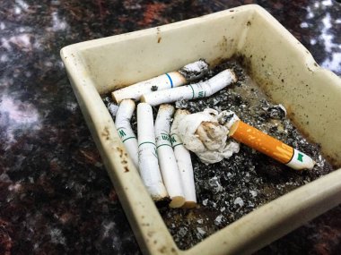 Kül tablası şeklinde bir kare içinde sigara izmaritleri olan ahşap bir masaya yerleştirilmiş..