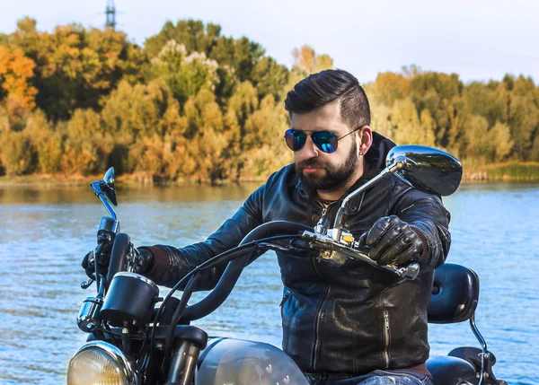 Biker homem vestindo uma jaqueta de couro e óculos de sol sentado em sua moto — Fotografia de Stock