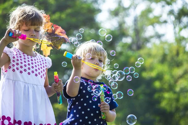 Two funny little sisters blowing soap bubbles outdoors — Stock Photo, Image