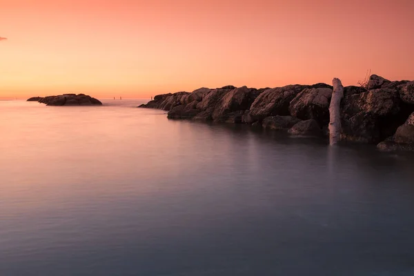 Pôr-do-sol laranja em frente ao mar e pedras na água — Fotografia de Stock