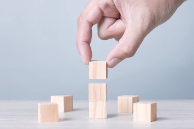 Three Wood Block Cubic stack with Hand on table Blue Tone Background. Free Copy Space.