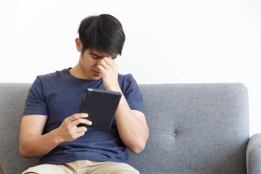 Koltukta otururken tablet kullanan ciddi bir adam. Kopyalama uzayı. Takas. EVLİK WFH Konseptinden Çalışma.