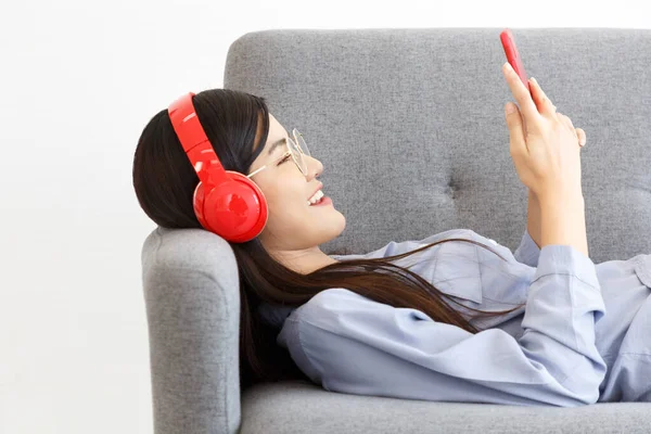 Neşeli Asyalı, kablosuz kulaklık takan akıllı telefondan müzik dinleyen neşeli kadının yan görüntüsü kanepeye uzandı..