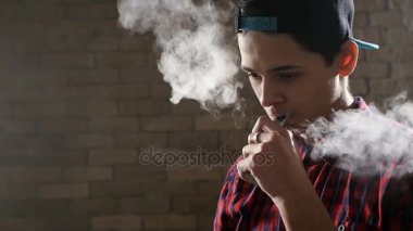 Kahverengi saçlı on dokuz yaşında bir çocuk kendini eğlenceli bir e-sigara kullanma ve onun ağzı ve burnu kalın duman gönderme vaping başlar