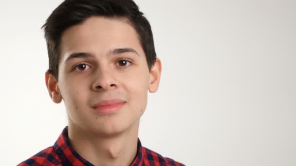 Ein neunzehnjähriger Junge aus Osteuropa zwinkert zuerst und lächelt dann, zeigt seine emotionale und glückliche Art, gekleidet in ein kariertes Hemd, während er in einem Studio ist — Stockvideo