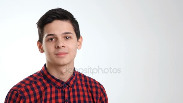 Ein smarter neunzehnjähriger Junge mit cremegeschnittenem Haarschnitt und dunkelbraunen Haaren, bekleidet mit kariertem Hemd, lächelt plötzlich und hält die Lachausbrüche zurück, im Studio — Stockvideo