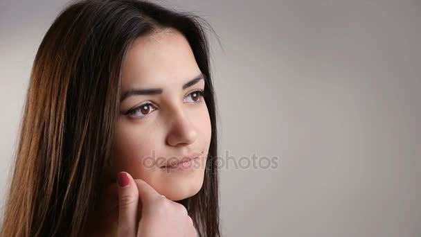 Uma linda menina de dezoito anos acaricia sua pele lisa, usando cosméticos, olha para uma câmera, sorri, toca seu longo cabelo castanho escuro solto, mostrando sua esplêndida manicure vermelha no estúdio — Vídeo de Stock