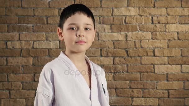 Een zeven jaar oude jongen, gekleed in kimono, glimlacht licht in studio met een bakstenen muur — Stockvideo