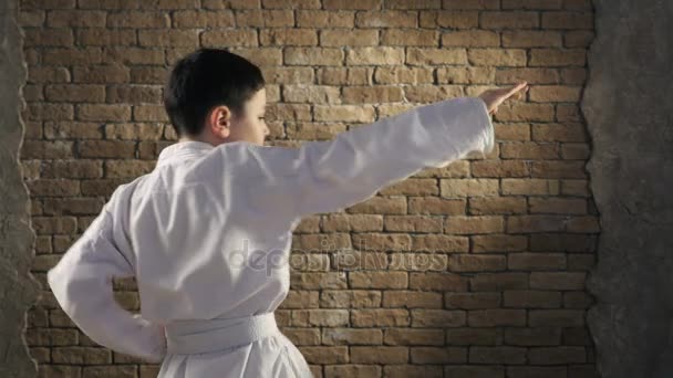 Un giovane karateka si alza in piedi di profilo e allena un colpo di mano coltello in studio — Video Stock