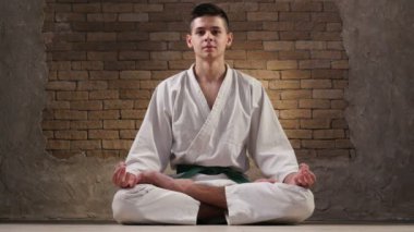 Genç oğlan beyaz karate kimono içinde Lotus poz oturur ve derin derin düşünür
