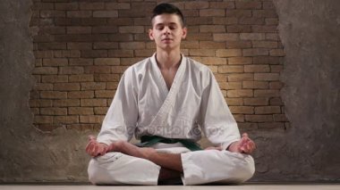 Bir on sekiz yaşındaki sporcu bir karate kimono içinde Lotus poz oturur ve derin derin düşünür 