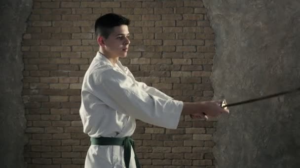 Um karateka jovem pratica artes marciais orientais e uso de katana em estúdio — Vídeo de Stock