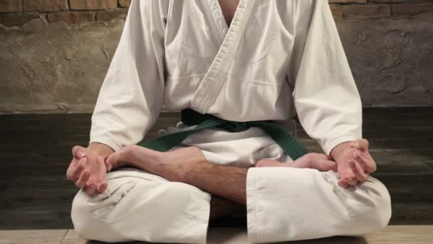 A young karateka meditates while sitting in Lotus pose in studio — Stock Video