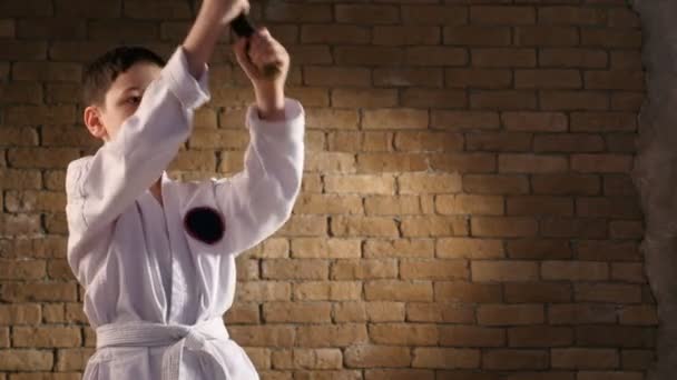 Un pequeño luchador entrena su katana hacia abajo, vestido con un kimono tradicional — Vídeos de Stock