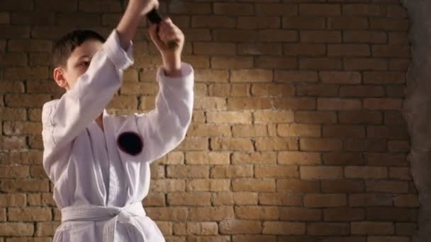 Een kleine vechter treinen zijn katana neerwaartse stakingen, gekleed in een traditionele kimono — Stockvideo