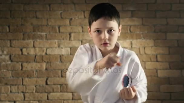 Seorang anak kecil berlatih memukul dengan tangannya, mengenakan kimono karate putih — Stok Video