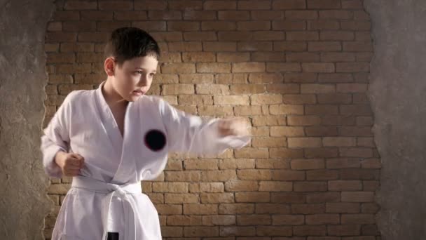 Молодий спортсмен, одягнений у традиційне кімоно, тренує свої ручні удари в студії — стокове відео