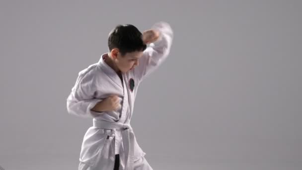 Ein junger Karateka steht im Profil und trainiert zwei Selbstverteidigungsblöcke im Studio — Stockvideo