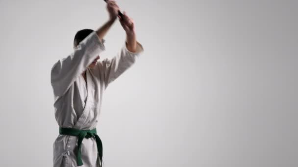 Katana utilizzo ad un allenamento di un giovane sportivo in kimono bianco in studio — Video Stock
