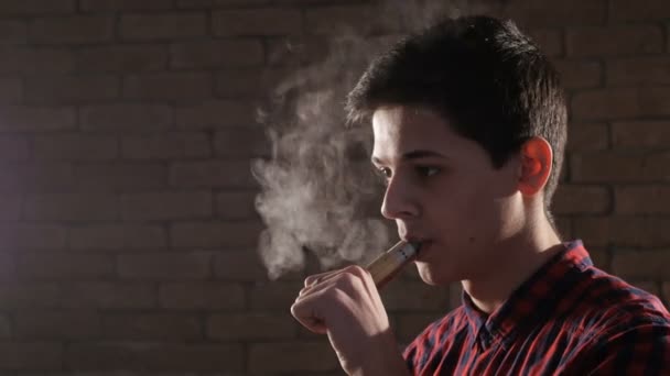Мальчик-подросток с электронной сигаретой развлекает и делает 15 маленьких колец дыма, стоя в профиль — стоковое видео