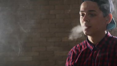 Genç çocuk üç çeyrek bir şekilde duruyor ve bir stüdyoda bir e-sigara içiyor