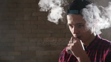 Genç genç çocuk üç çeyrek bir şekilde duruyor ve bir e-sigara içiyor