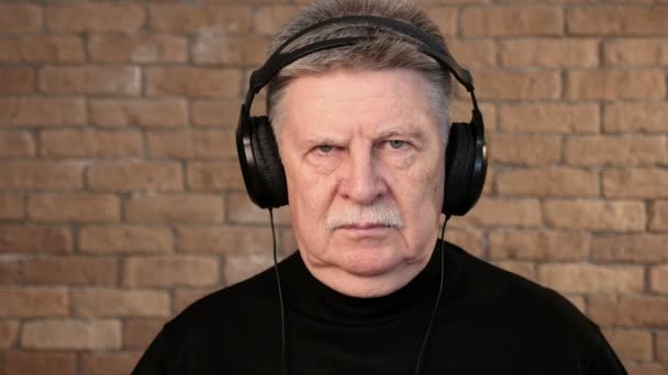 Seorang pria berkepala abu-abu menggelengkan kepalanya sambil mendengarkan musik di headphone — Stok Video