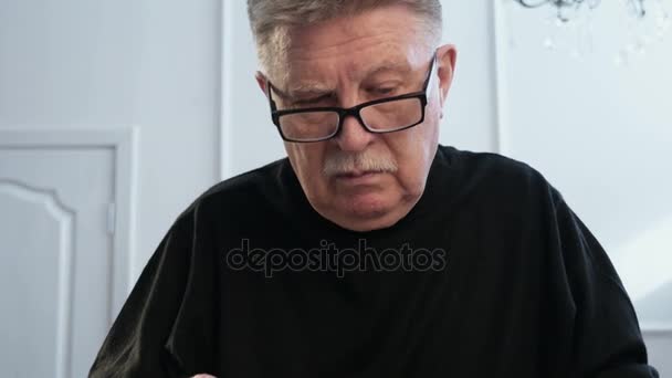 Ein grauhaariger Mann erkundet mit einer Handlinse einen alten Text auf gelben Seiten — Stockvideo