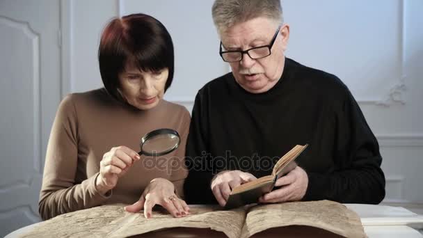 Два пожилых человека исследуют старую еврейскую рукопись, используя ручной объектив и книгу — стоковое видео