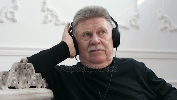 Un hombre de cabeza gris disfruta de su vida y escucha la música a través de auriculares — Vídeos de Stock