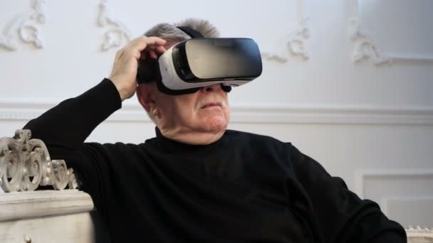 Un hombre de cabeza gris mantiene un HMD en su cabeza y observa algún juego — Vídeo de stock