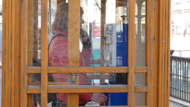 Mujer joven entra en una cabina de telefonía en una calle de la ciudad y comienza a llamar — Vídeo de stock