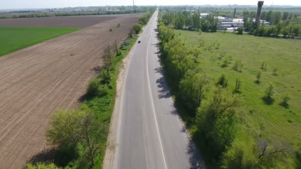 Tiro aéreo de uma estrada que se estende por um arado e campos verdes na primavera — Vídeo de Stock