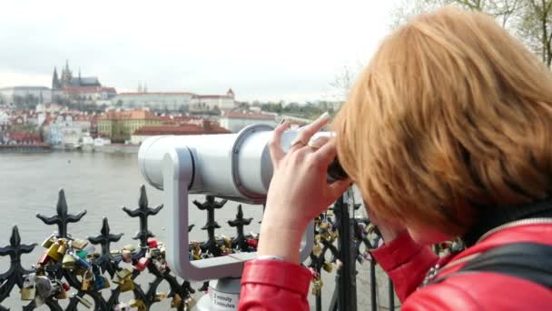 Fiatal nő keres egy távcső: egy pictiresque Prága folyó quay — Stock videók